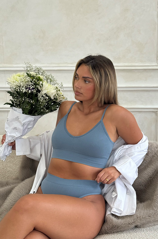 Woman in a blue seamless lounge set bra and shorts sitting on a couch holding flowers.