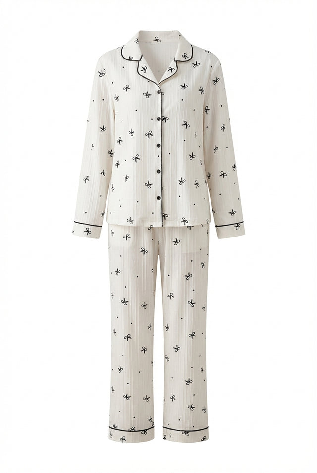 Ivory bow print pyjama set with button-through long sleeve shirt, contrast piping and matching trousers. Image is product cut out