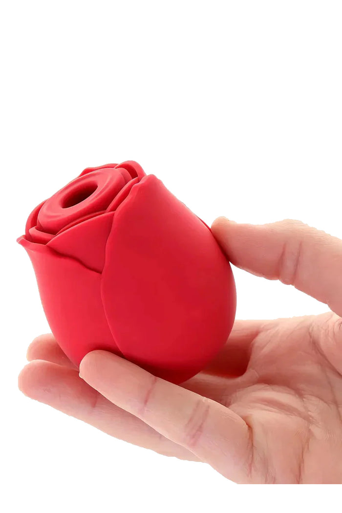 Red silicone rose-shaped suction vibrator held in hand, showing detailed petal design and clitoral tip.